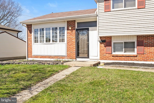 doorway to property with brick siding, a shingled roof, and a lawn