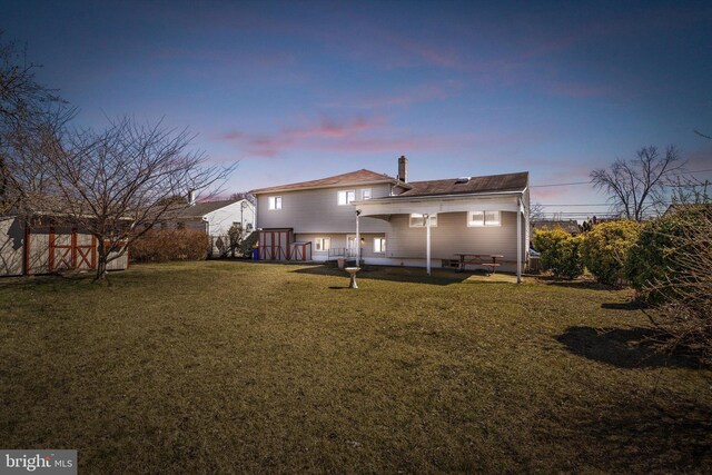 back of house at dusk with fence and a lawn