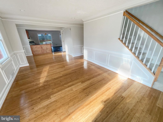 unfurnished living room with stairway, wood finished floors, ornamental molding, and a decorative wall