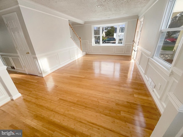 unfurnished living room with a textured ceiling, stairs, a decorative wall, and light wood-type flooring
