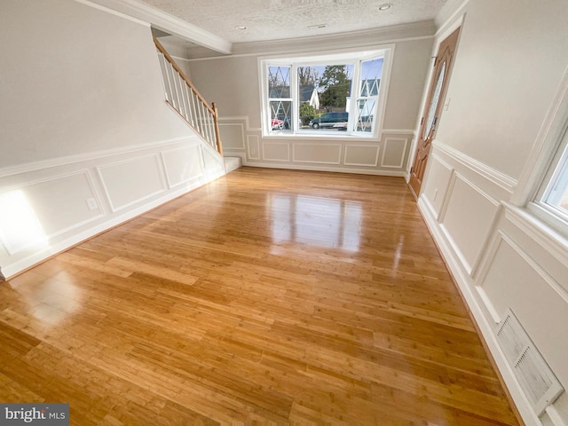 spare room featuring light wood-style flooring, a decorative wall, visible vents, and stairway