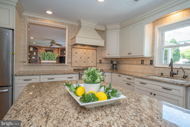 kitchen with ornamental molding, custom exhaust hood, white cabinetry, a sink, and appliances with stainless steel finishes
