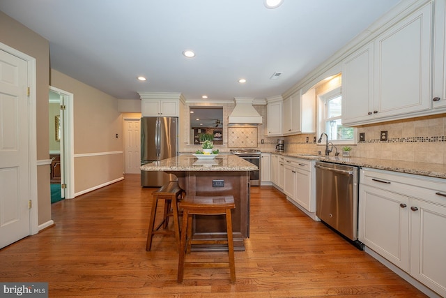 kitchen with decorative backsplash, a kitchen island, appliances with stainless steel finishes, a sink, and premium range hood