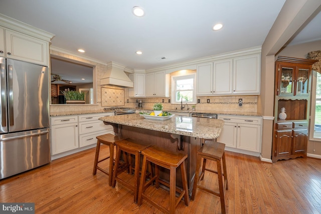kitchen with decorative backsplash, a sink, custom exhaust hood, a breakfast bar, and stainless steel appliances