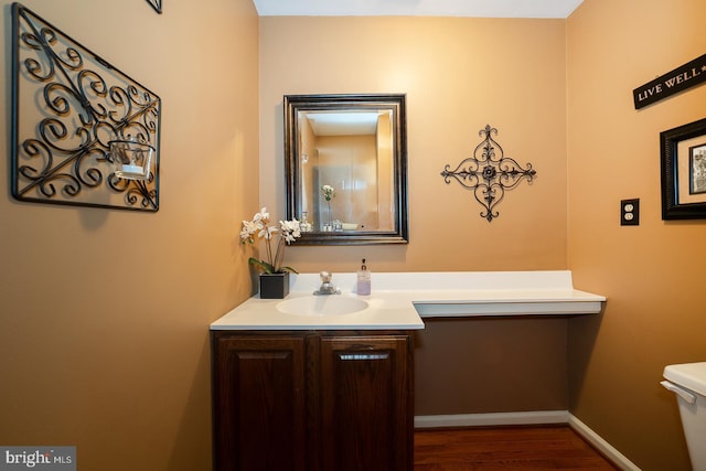 half bathroom with toilet, baseboards, wood finished floors, and vanity