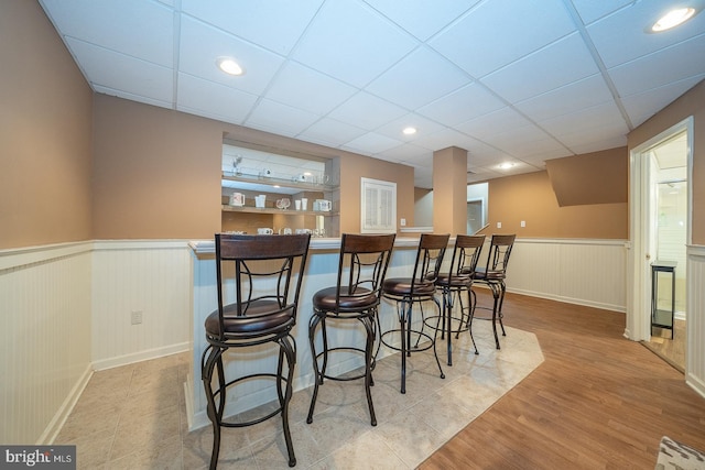 bar featuring a wainscoted wall, a drop ceiling, recessed lighting, and wood finished floors