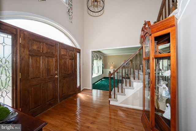 foyer entrance with baseboards, wood finished floors, a notable chandelier, and stairway