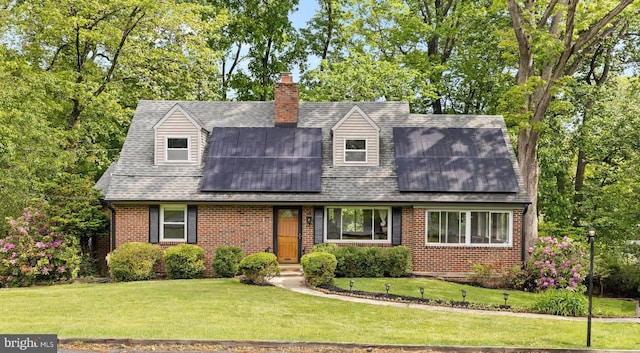 cape cod home featuring brick siding, roof mounted solar panels, a front lawn, roof with shingles, and a chimney