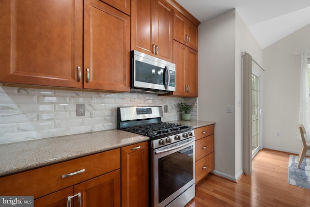 63 Woodleigh Ln, Stafford, VA 22556 - kitchen featuring brown cabinets, stainless steel appliances, light wood-style floors, light stone counters, and backsplash