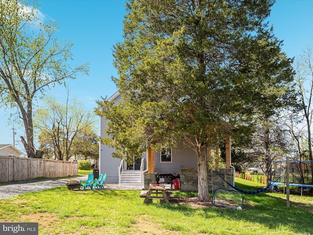 back of house with entry steps, a trampoline, fence, and a lawn