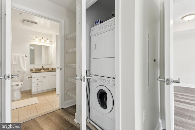 clothes washing area featuring a sink, light wood-style flooring, stacked washer / dryer, laundry area, and baseboards
