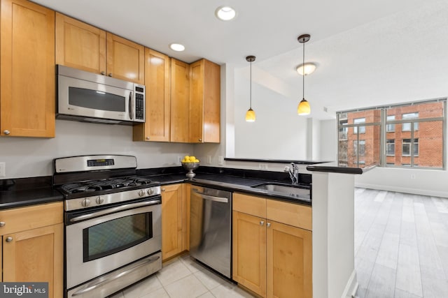 kitchen with a sink, dark countertops, a peninsula, and appliances with stainless steel finishes