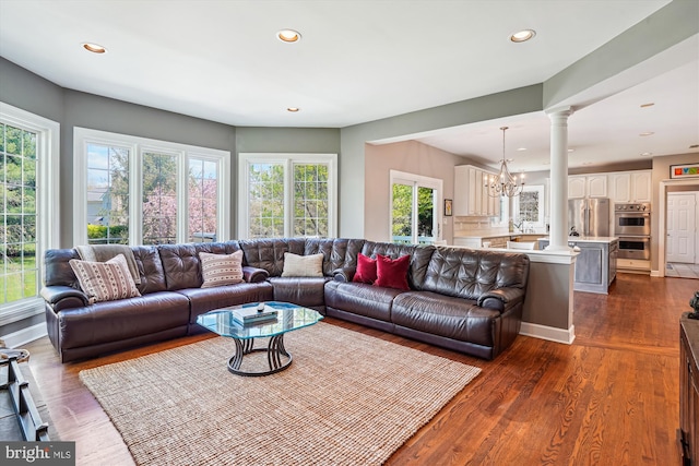 living room featuring recessed lighting, dark wood finished floors, decorative columns, and an inviting chandelier