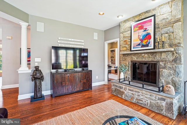 living area with a fireplace, wood finished floors, baseboards, and decorative columns