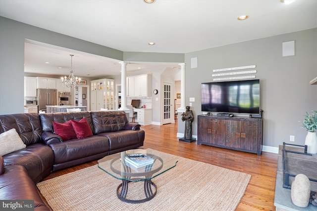 living area featuring a notable chandelier, light wood-style flooring, recessed lighting, and decorative columns