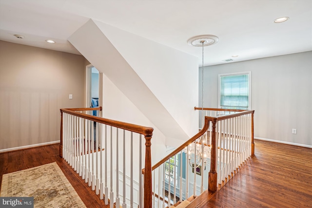 corridor featuring recessed lighting, wood finished floors, baseboards, and an upstairs landing