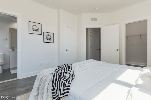 bedroom with a closet, baseboards, ensuite bath, visible vents, and dark wood finished floors