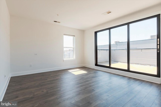 empty room with dark wood-type flooring, baseboards, and visible vents
