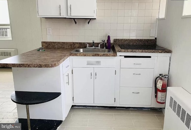 kitchen with white cabinetry, backsplash, a sink, dark countertops, and radiator heating unit
