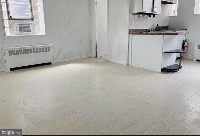 unfurnished living room with cooling unit, radiator, and light wood-style floors
