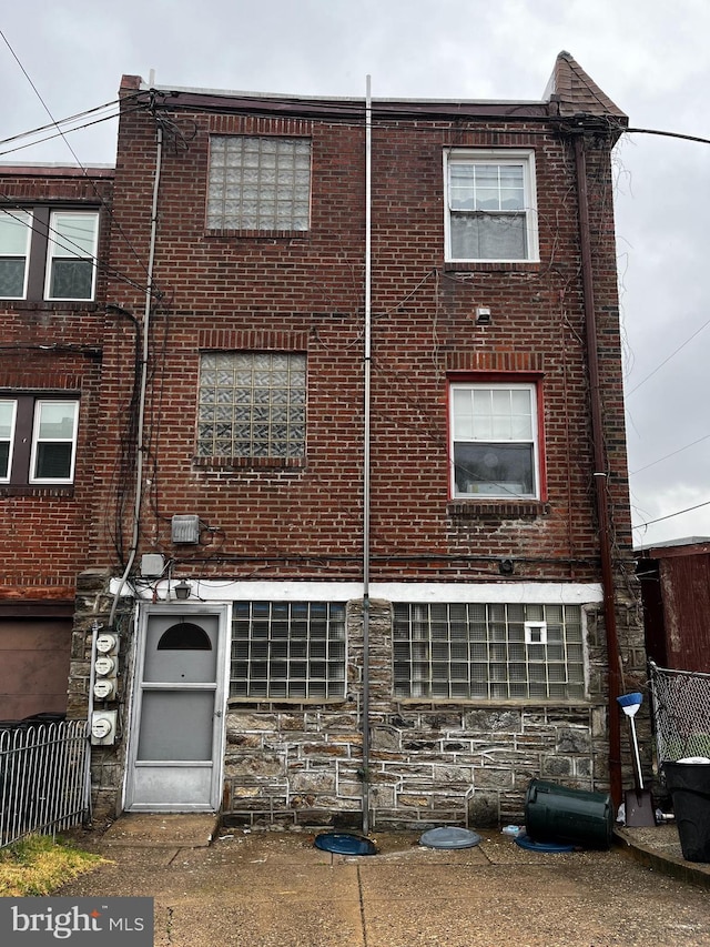 back of property with stone siding, brick siding, and fence