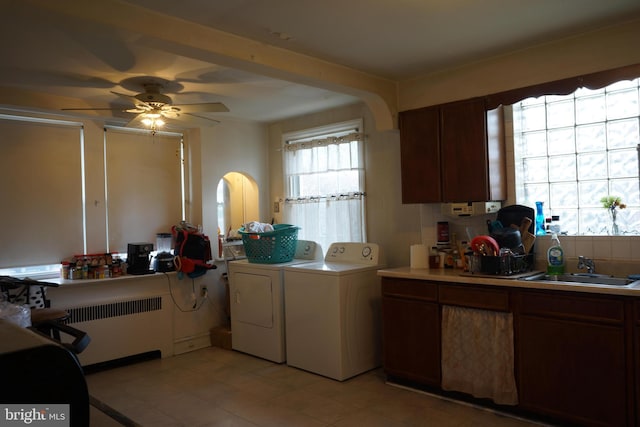 clothes washing area with radiator, separate washer and dryer, a sink, arched walkways, and laundry area