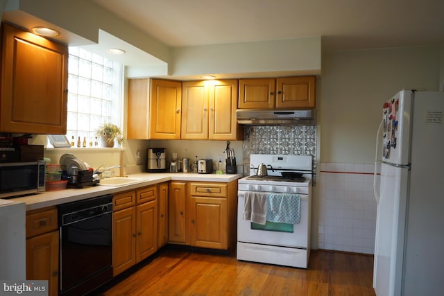 kitchen with light countertops, white appliances, under cabinet range hood, a sink, and wood finished floors