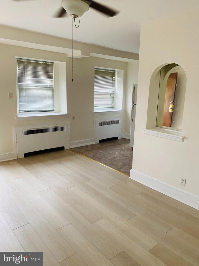 spare room with a ceiling fan, radiator, baseboards, and wood finished floors