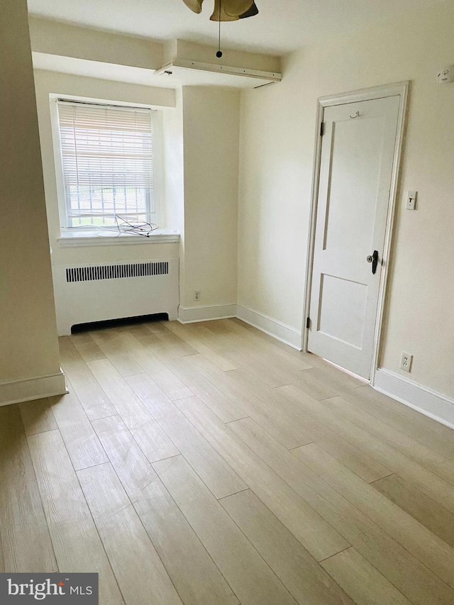 spare room with baseboards, ceiling fan, wood finished floors, and radiator heating unit
