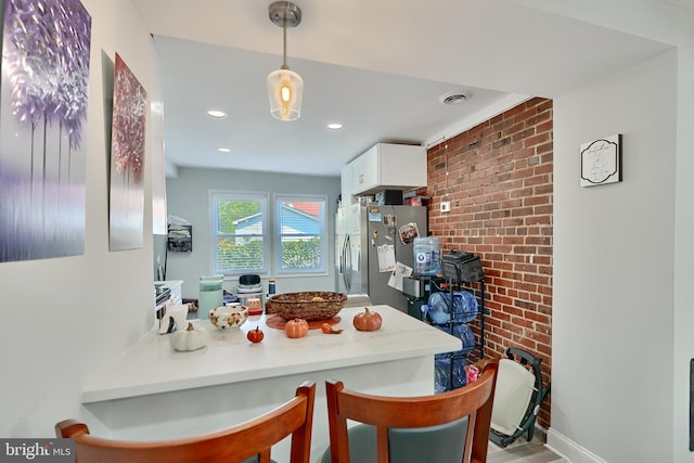 kitchen with freestanding refrigerator, a peninsula, a kitchen breakfast bar, white cabinetry, and hanging light fixtures