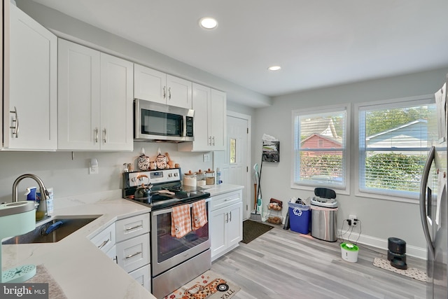 kitchen with appliances with stainless steel finishes, light stone countertops, a sink, white cabinets, and recessed lighting