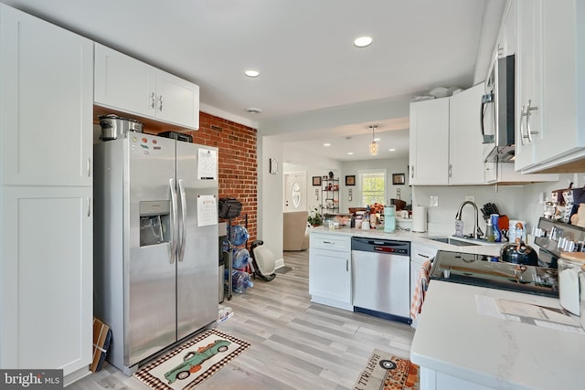 kitchen featuring brick wall, appliances with stainless steel finishes, a sink, recessed lighting, and white cabinetry