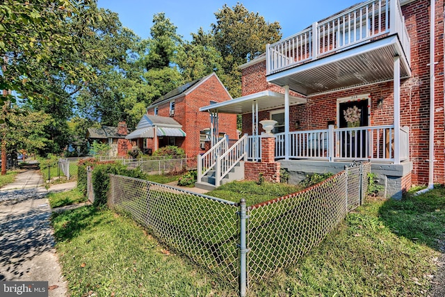 back of house with a porch, brick siding, fence private yard, and a balcony