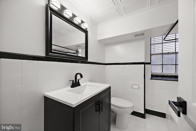 bathroom with crown molding, wainscoting, vanity, toilet, and tile walls