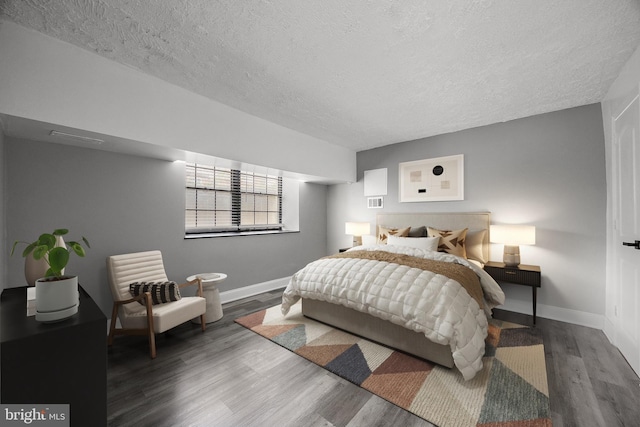 bedroom with baseboards, a textured ceiling, visible vents, and wood finished floors