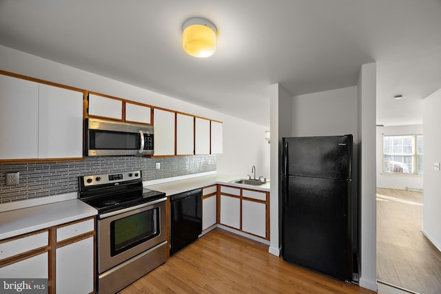 kitchen with light wood-style floors, black appliances, light countertops, a sink, and decorative backsplash