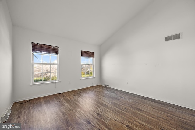 empty room featuring dark wood-style flooring, vaulted ceiling, and visible vents