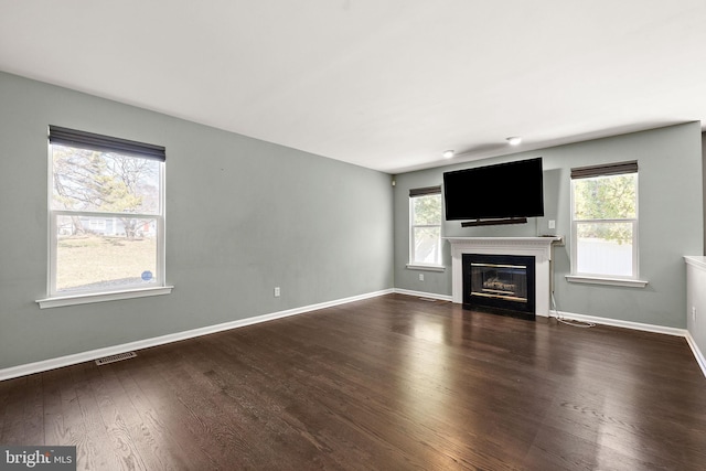 unfurnished living room with baseboards, visible vents, a fireplace with flush hearth, and wood finished floors