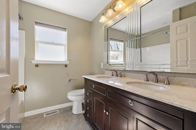 bathroom featuring double vanity, toilet, baseboards, and a sink