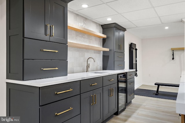 kitchen featuring open shelves, beverage cooler, baseboards, tasteful backsplash, and a sink