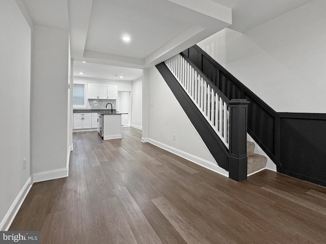 unfurnished living room featuring a sink, baseboards, stairs, and dark wood-style flooring