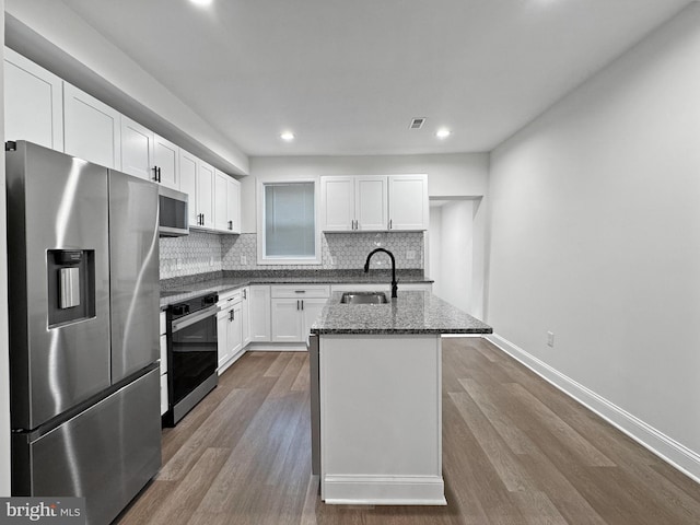 kitchen featuring dark stone countertops, dark wood-style flooring, white cabinetry, stainless steel appliances, and decorative backsplash