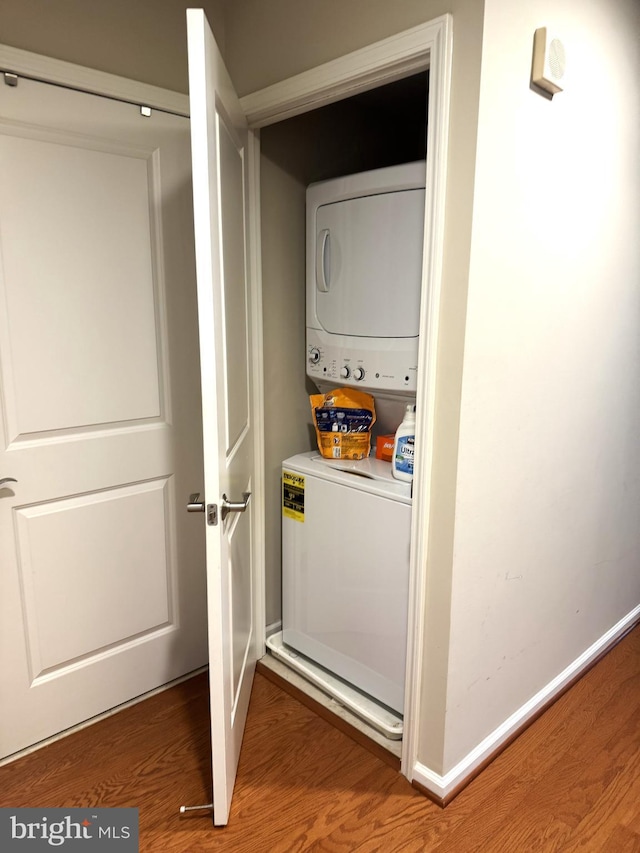 laundry area with baseboards, laundry area, stacked washer / dryer, and wood finished floors
