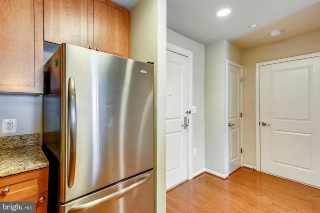 kitchen with freestanding refrigerator, light wood finished floors, light stone countertops, and brown cabinets