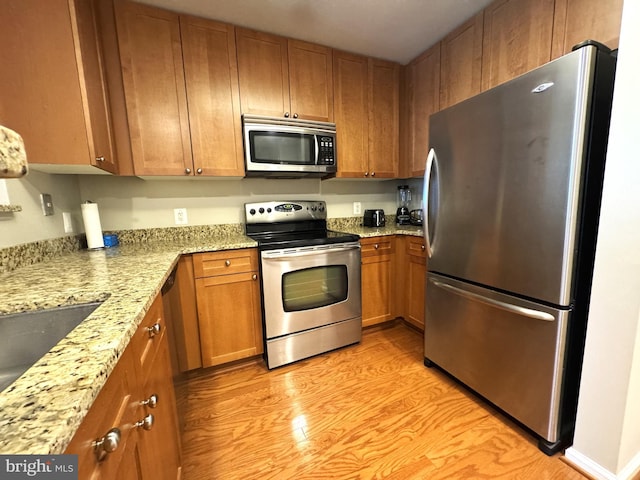 kitchen featuring stainless steel appliances, brown cabinetry, light stone countertops, and light wood-style flooring