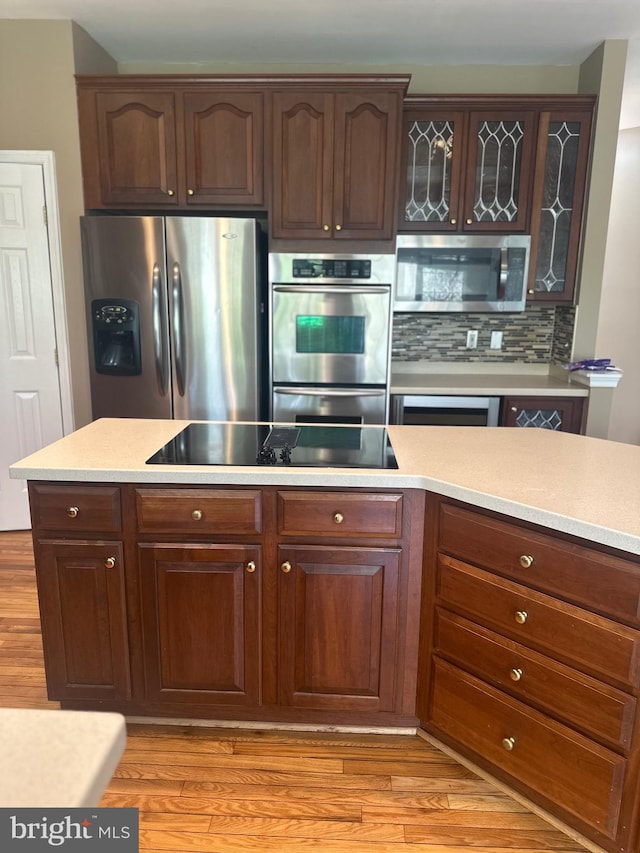 kitchen with light wood finished floors, light countertops, stainless steel appliances, backsplash, and glass insert cabinets