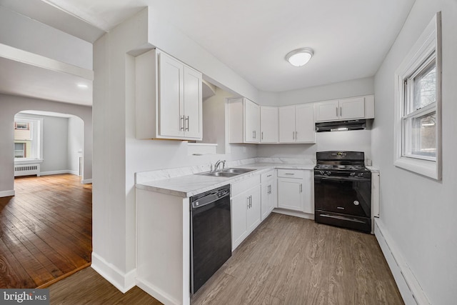 kitchen with radiator, a sink, under cabinet range hood, black appliances, and wood finished floors