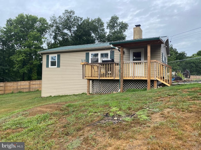 view of front of home featuring a front yard, a deck, fence, and a chimney