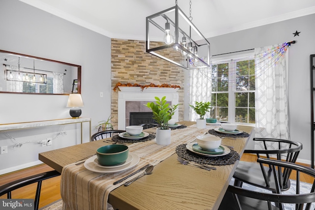dining space with baseboards, ornamental molding, a chandelier, a tiled fireplace, and wood finished floors