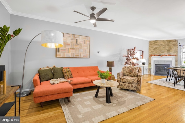 living room featuring a tiled fireplace, ceiling fan, ornamental molding, and wood finished floors